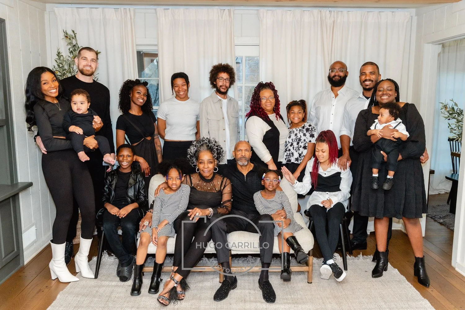 A large family group posing indoors with some members standing and others seated, including children and adults of different ages and ethnicities.