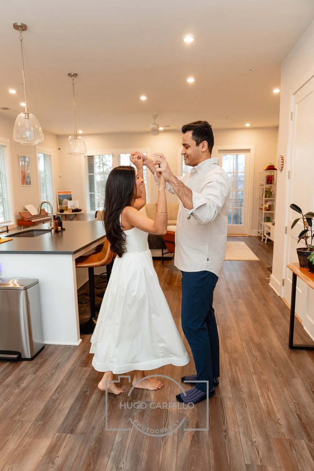 A couple dancing and smiling in a modern, well-lit kitchen and living room area.