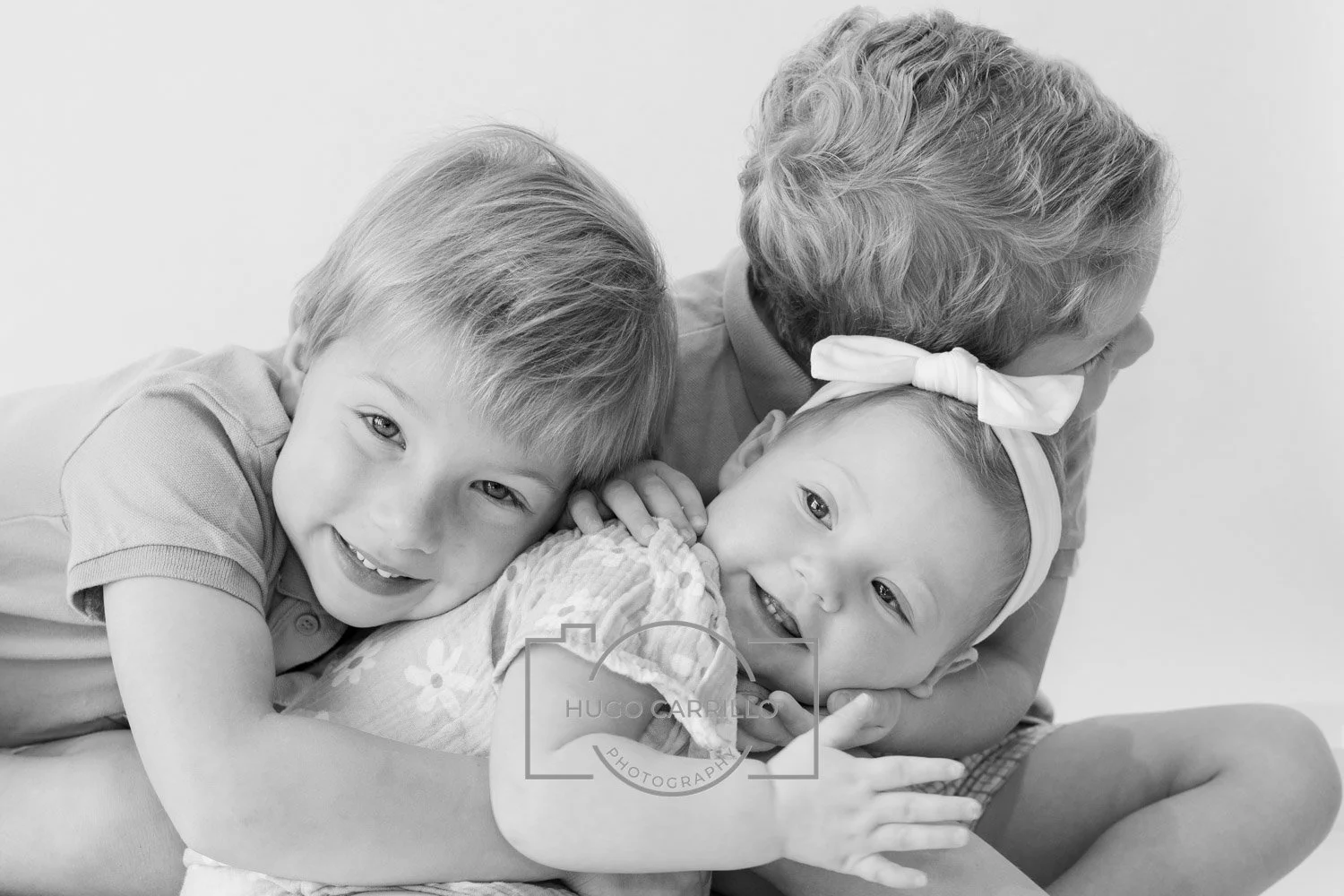 A black and white photo of a woman hugging two young children, one boy and one girl, all smiling and looking happy.