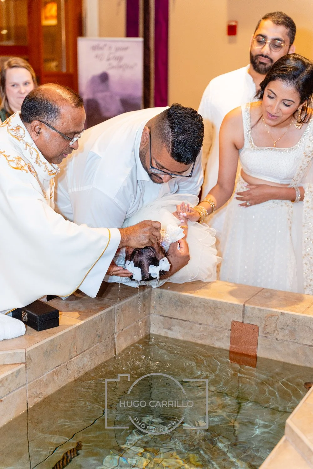 A group of people participating in a baptism ceremony, pouring water over a baby in a church setting.