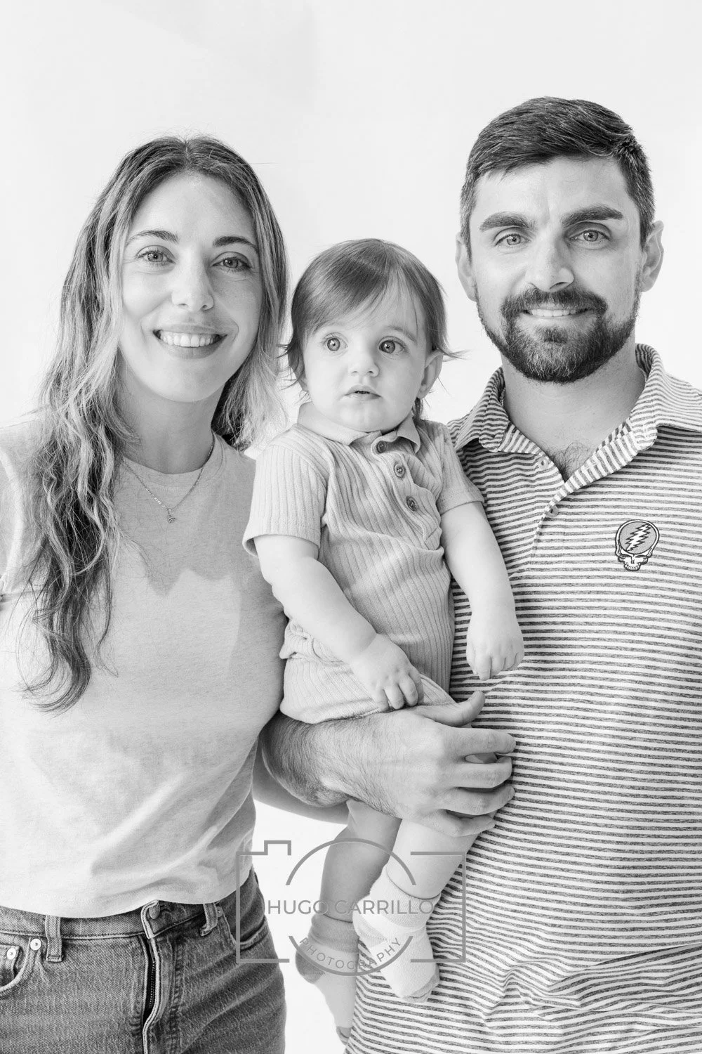 A black and white photo of a smiling woman and man holding a young child, all facing the camera against a plain background.