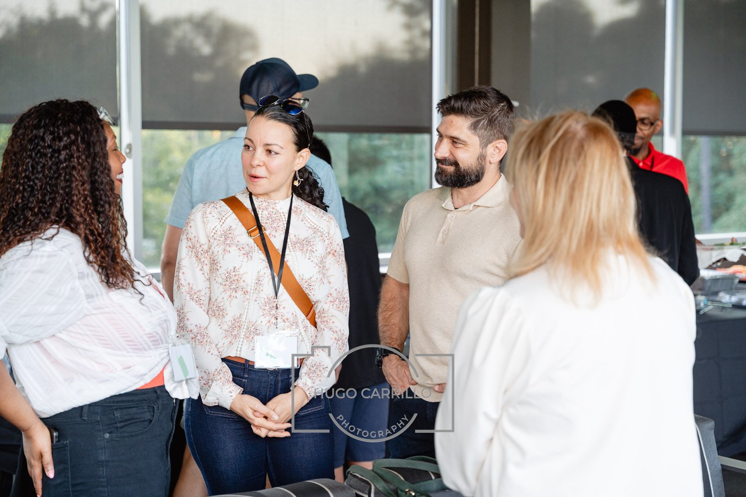 People talking and networking at a conference or event, with a woman in a white blouse and another woman with glasses and a lanyard engaged in conversation.