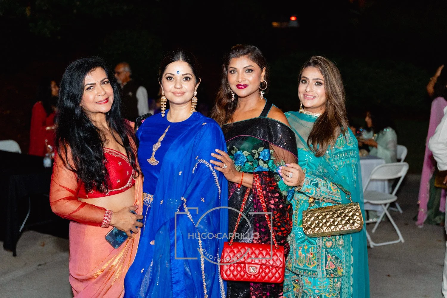Four women dressed in colorful traditional Indian attire posing for a photo at night at an outdoor event.