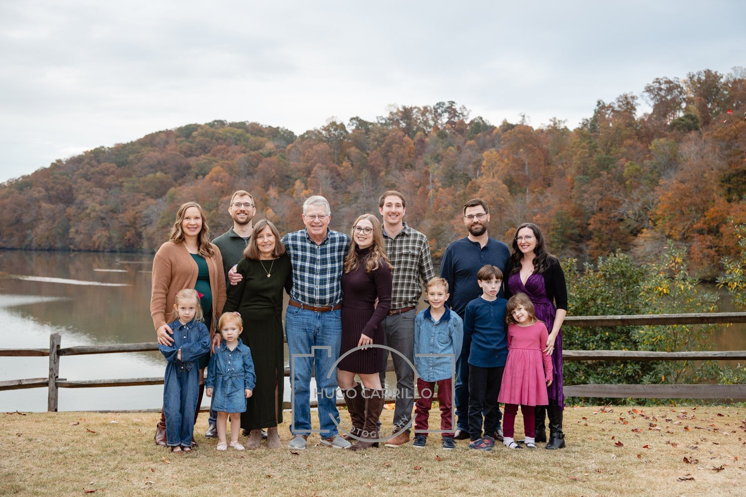 Family group photo outdoors near a lake and colored fall trees, including children and adults smiling.