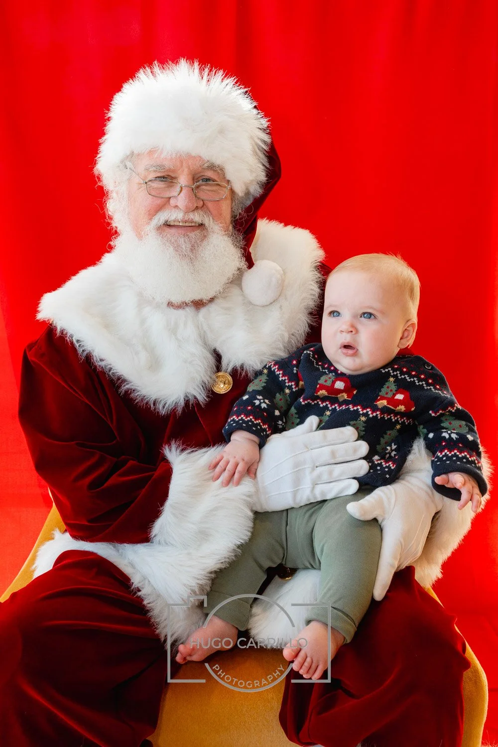 Santa Claus holding a baby in front of a red backdrop.