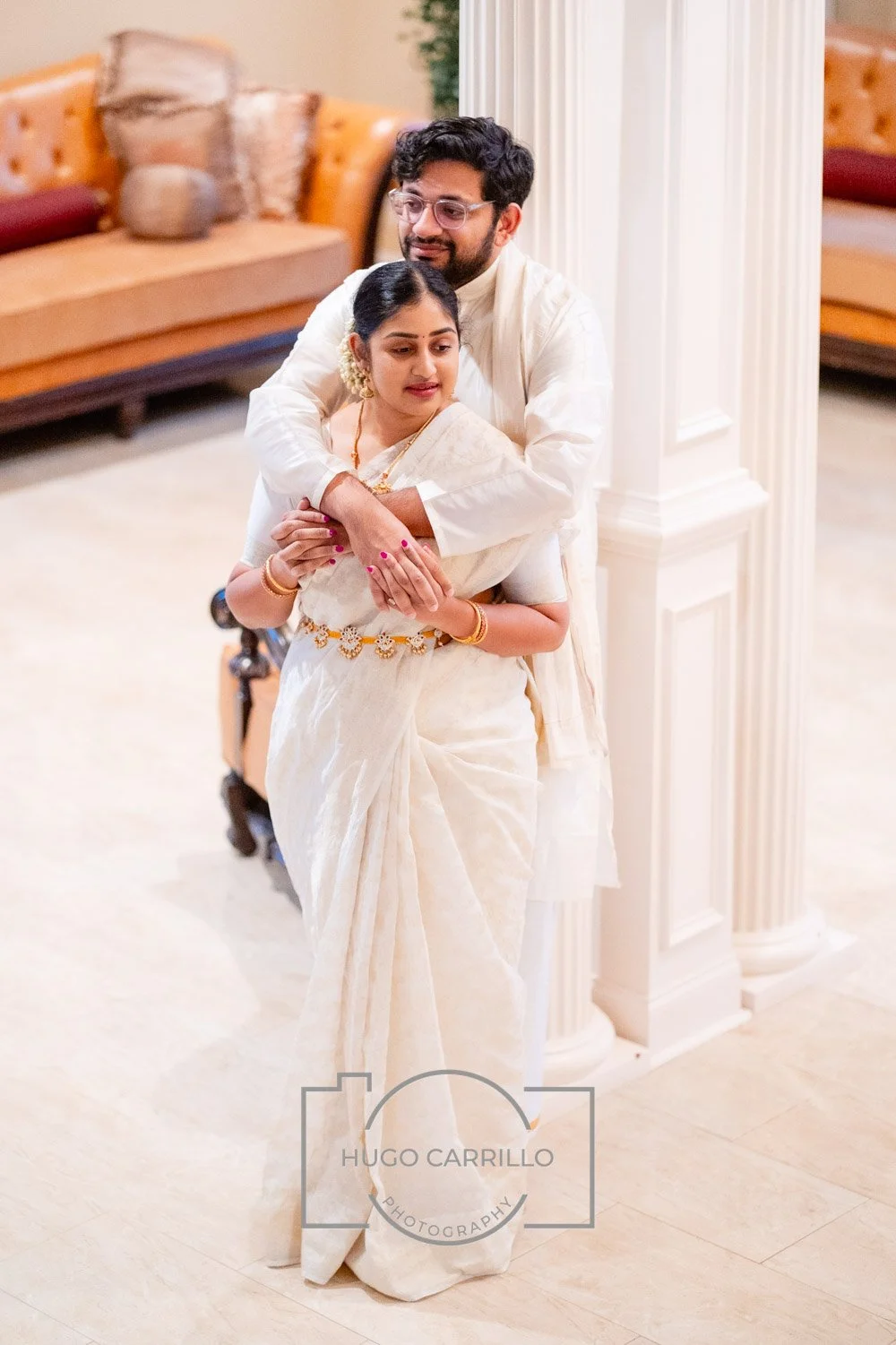 A man and woman in traditional Indian attire sharing a warm embrace in a warmly decorated living room.