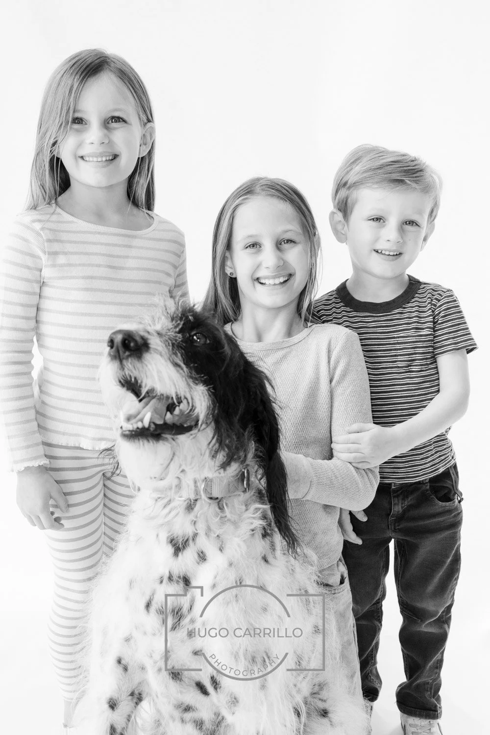 Three children and a dog in a studio portrait, all smiling, in black and white.