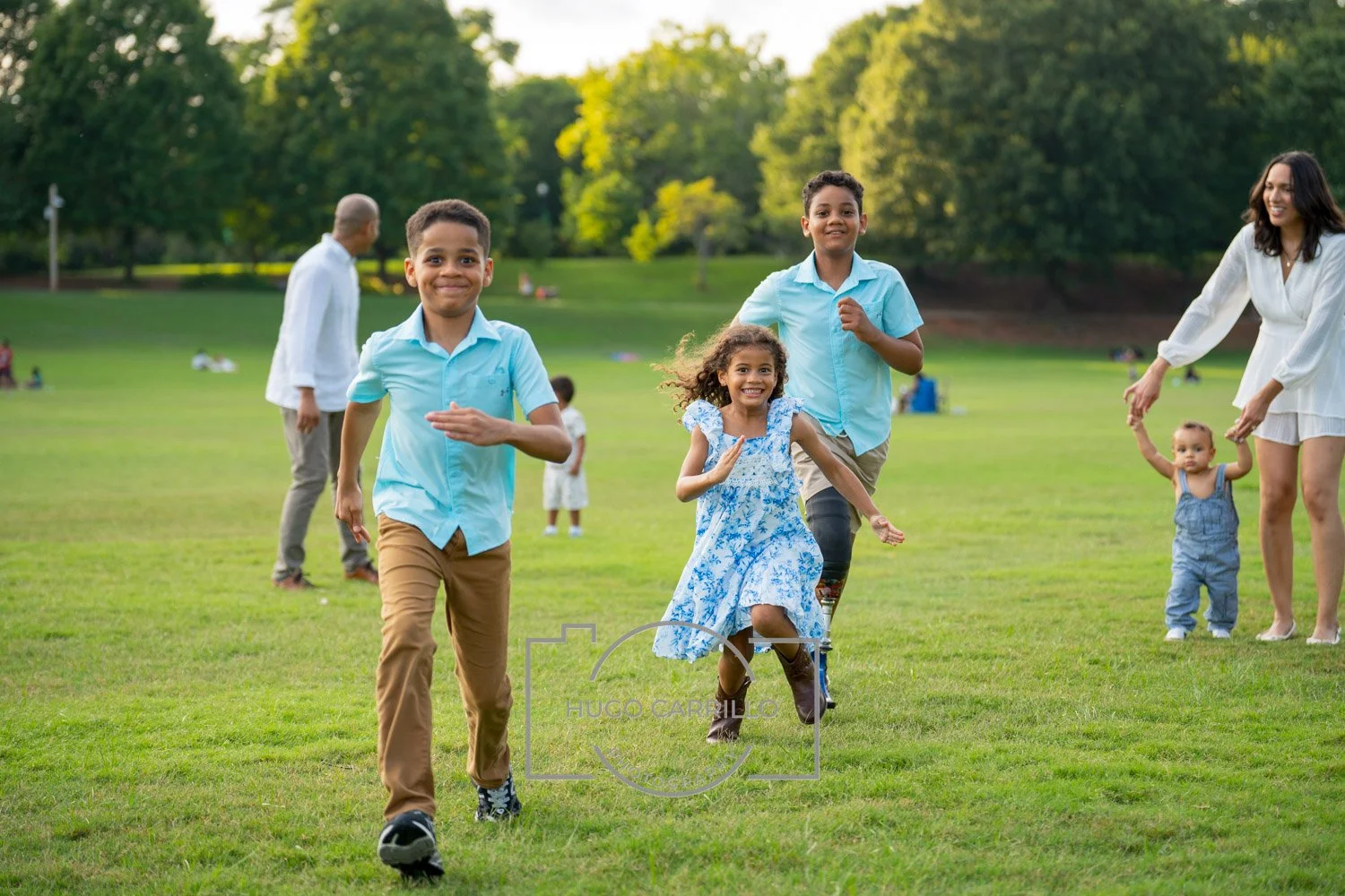 Smiling children and adults running and playing in a green park on a clear day.