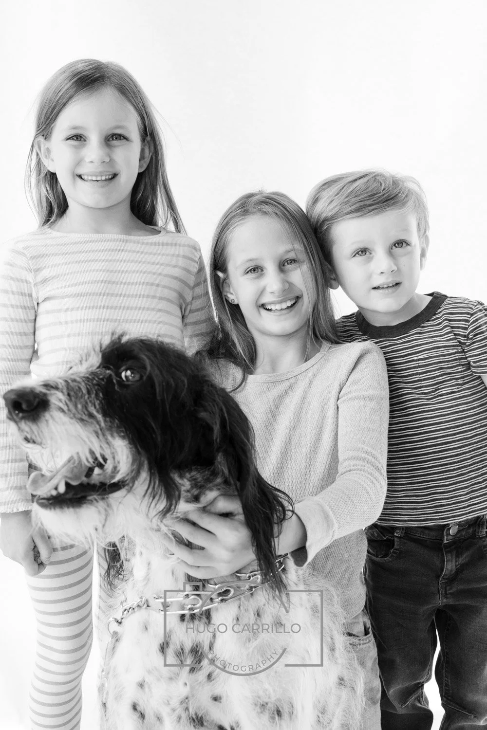 Three children and a dog in a black-and-white portrait. The children are smiling, and the dog is being held by one of the girls.