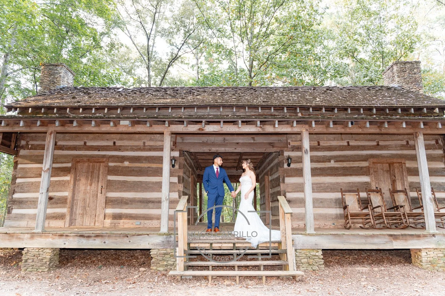 A bride and groom holding hands standing on the steps of a rustic wooden cabin surrounded by trees.