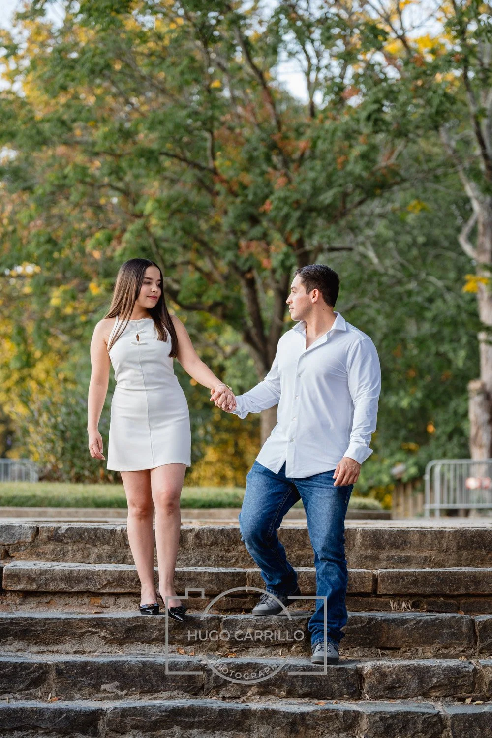 A man and woman holding hands on outdoor stone steps, with trees in the background, during daytime.