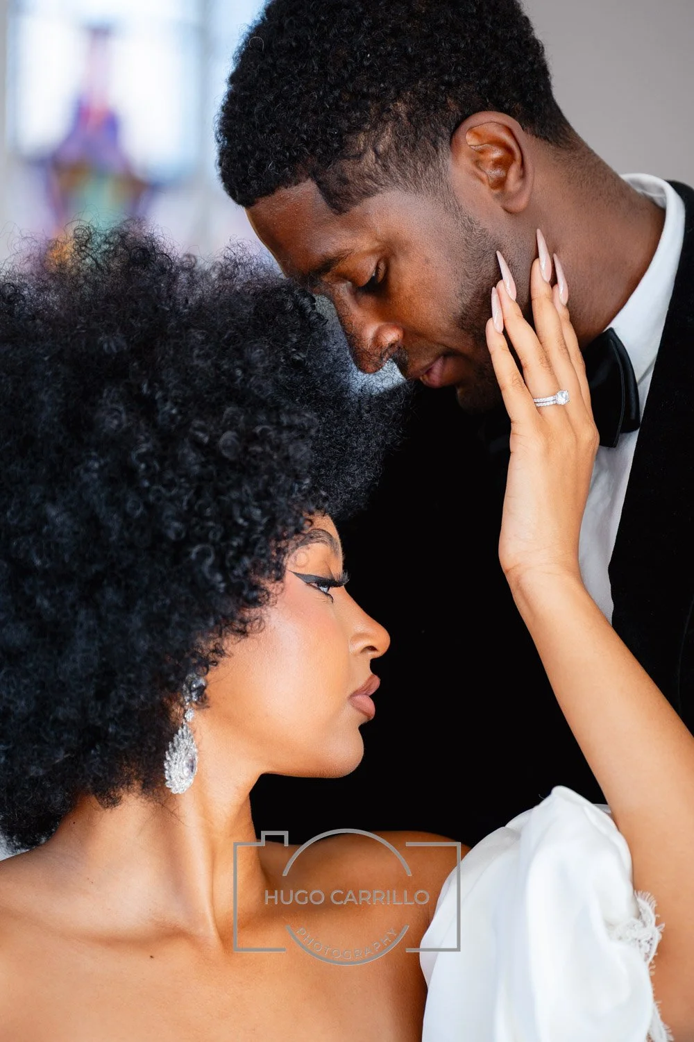 A couple in formal attire sharing an intimate moment, with foreheads touching and eyes closed, in a romantic setting.