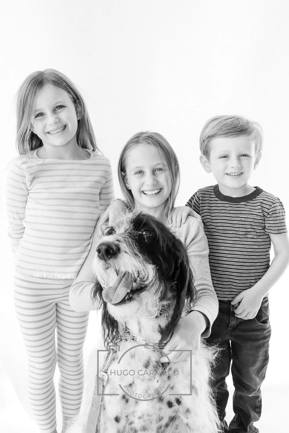 Three children and a dog smiling for a photo against a white background.