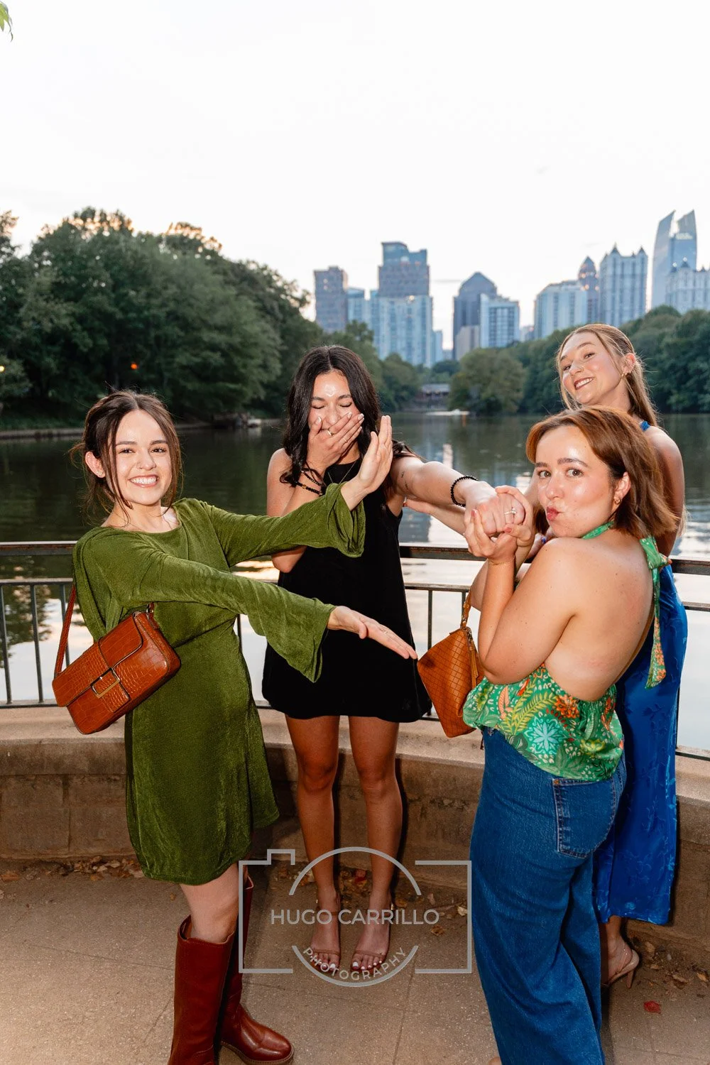 Four women celebrating and having fun by a river with a city skyline in the background.