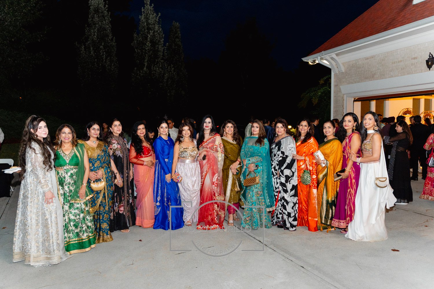 Group of women dressed in traditional and colorful Indian attire posing for a photo outside during an evening event.