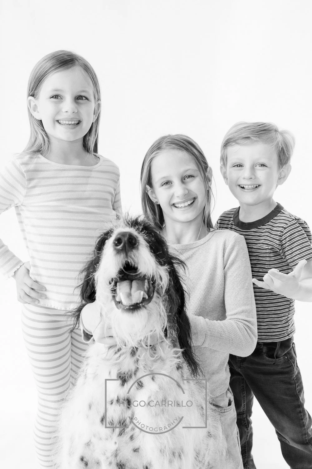 Three children and a dog smiling at the camera against a plain background, black and white photo.
