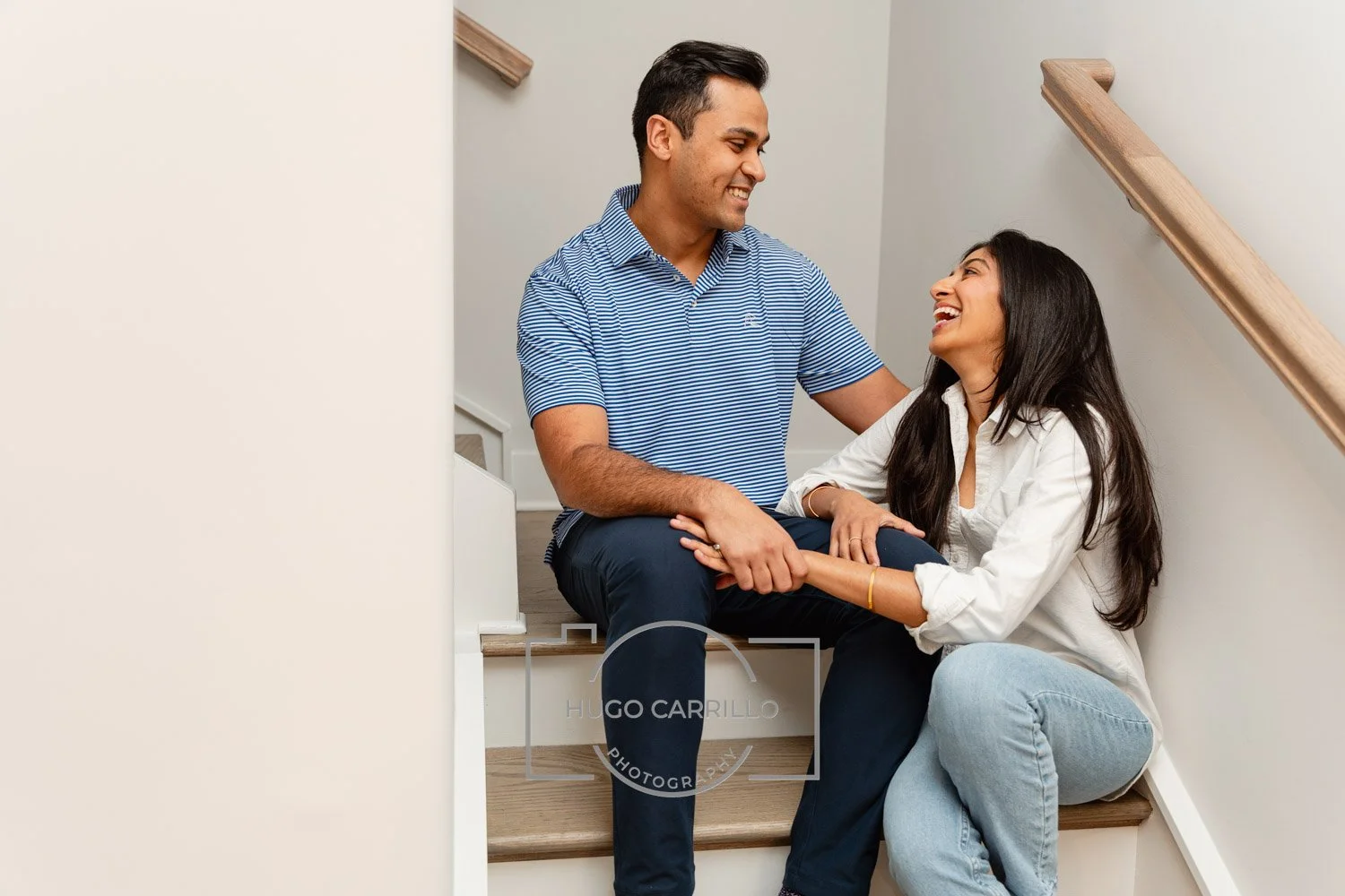 A happy couple sitting on a staircase, looking at each other and smiling, inside a home.