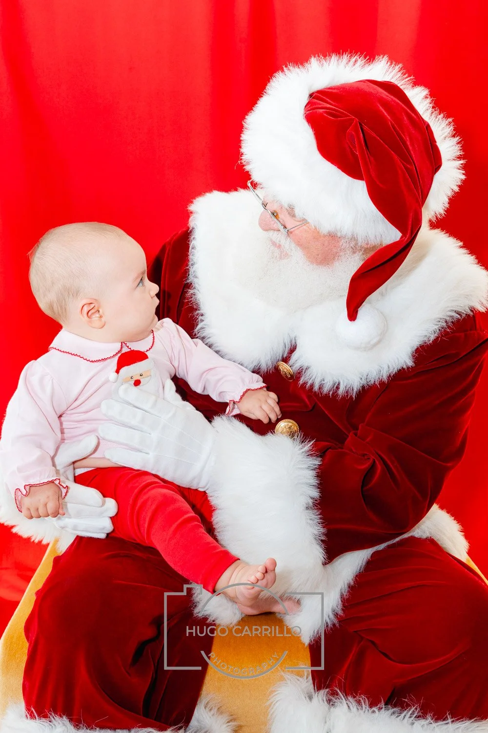 Santa Claus holding a baby girl with a red background.