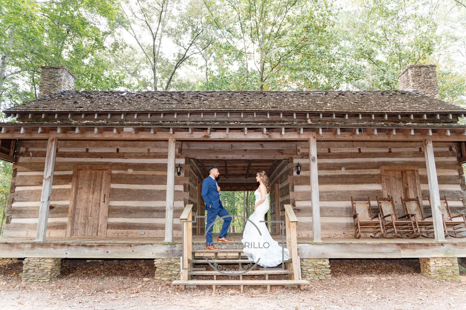 A couple in wedding attire standing on the steps of a rustic wooden cabin, surrounded by trees.