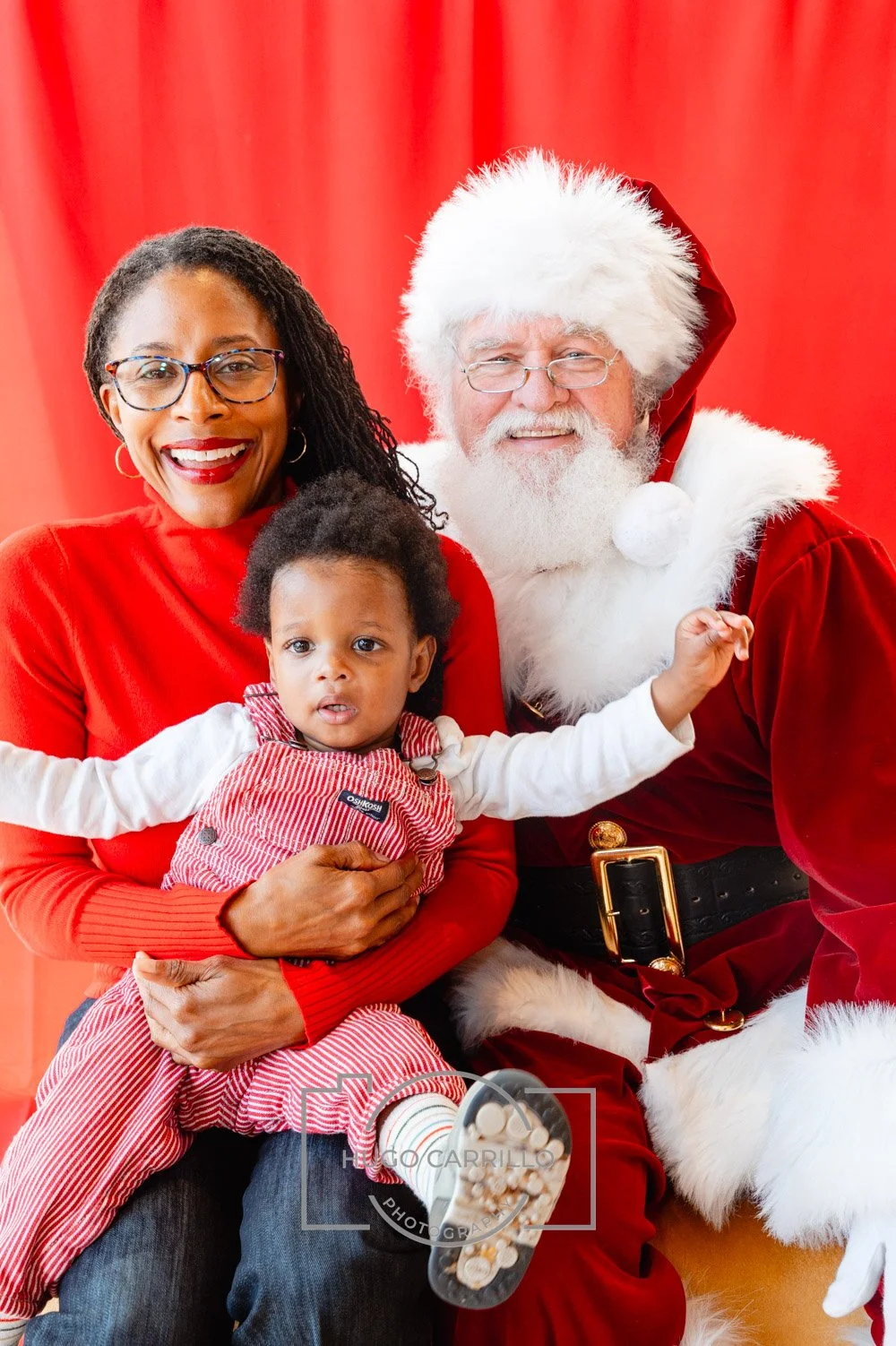 A family celebrating Christmas with a woman, a young girl, and Santa Claus in front of a red background.