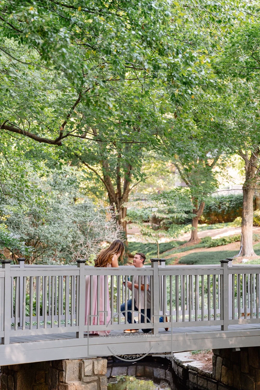 A man kneels to propose on a wooden park bridge