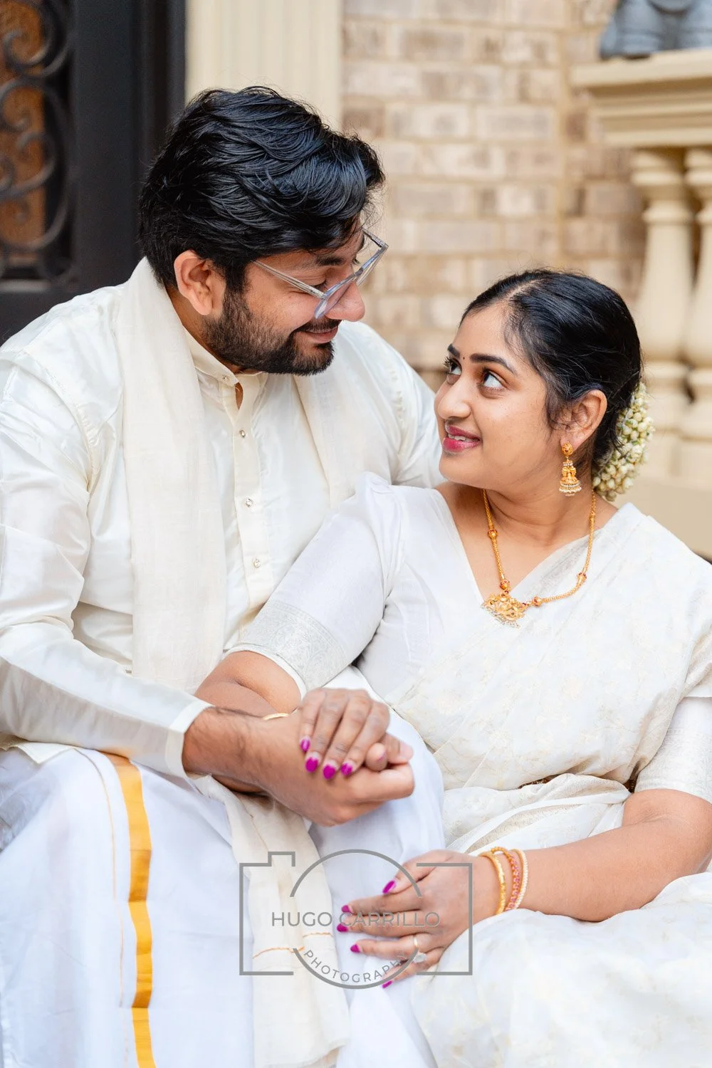 A man and woman dressed in traditional Indian attire sitting close and looking at each other affectionately.