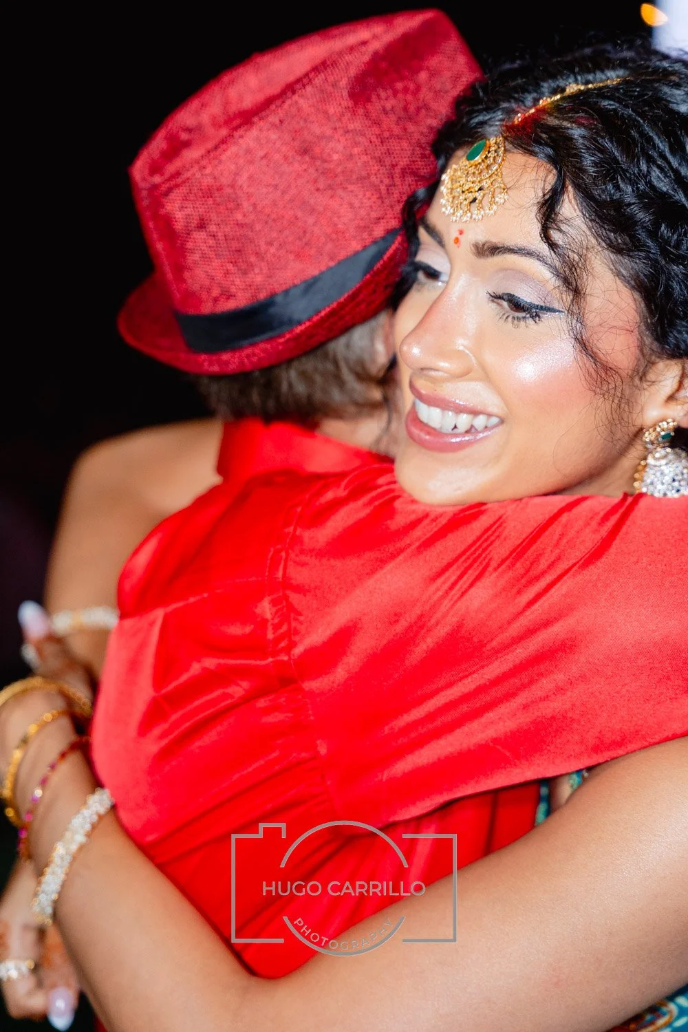 A woman with jewelry and traditional makeup hugging a person wearing a red hat and red outfit at a celebration or event.
