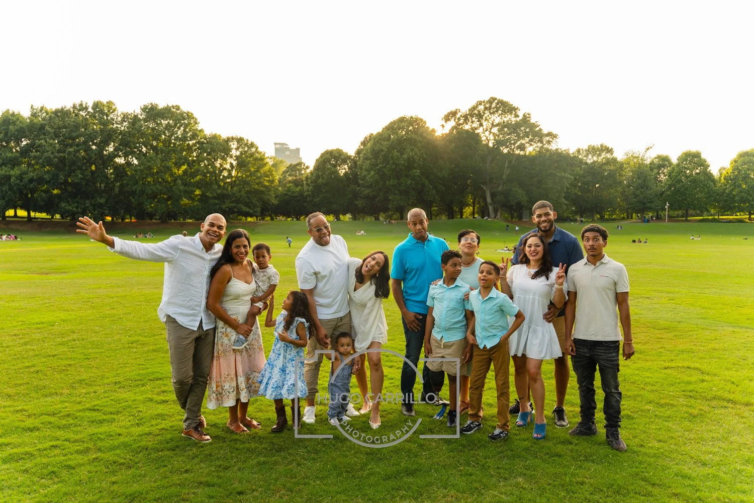 A large family group standing on a grassy park field during sunset, smiling and posing for a photo.