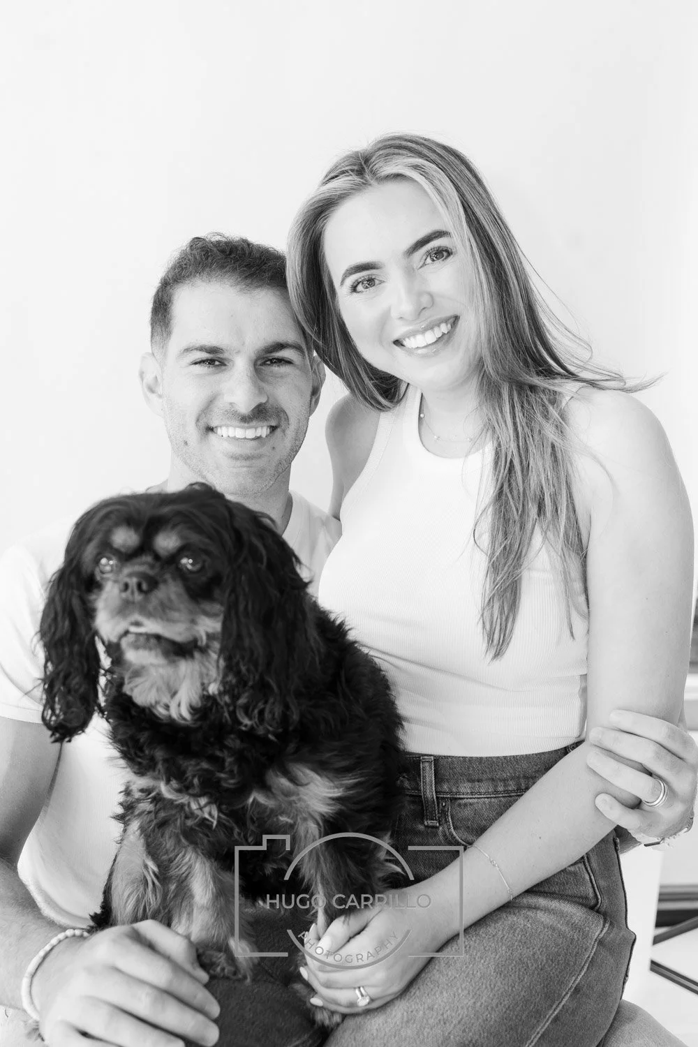 A happy couple with their black dog, smiling at the camera, in a well-lit indoor setting.