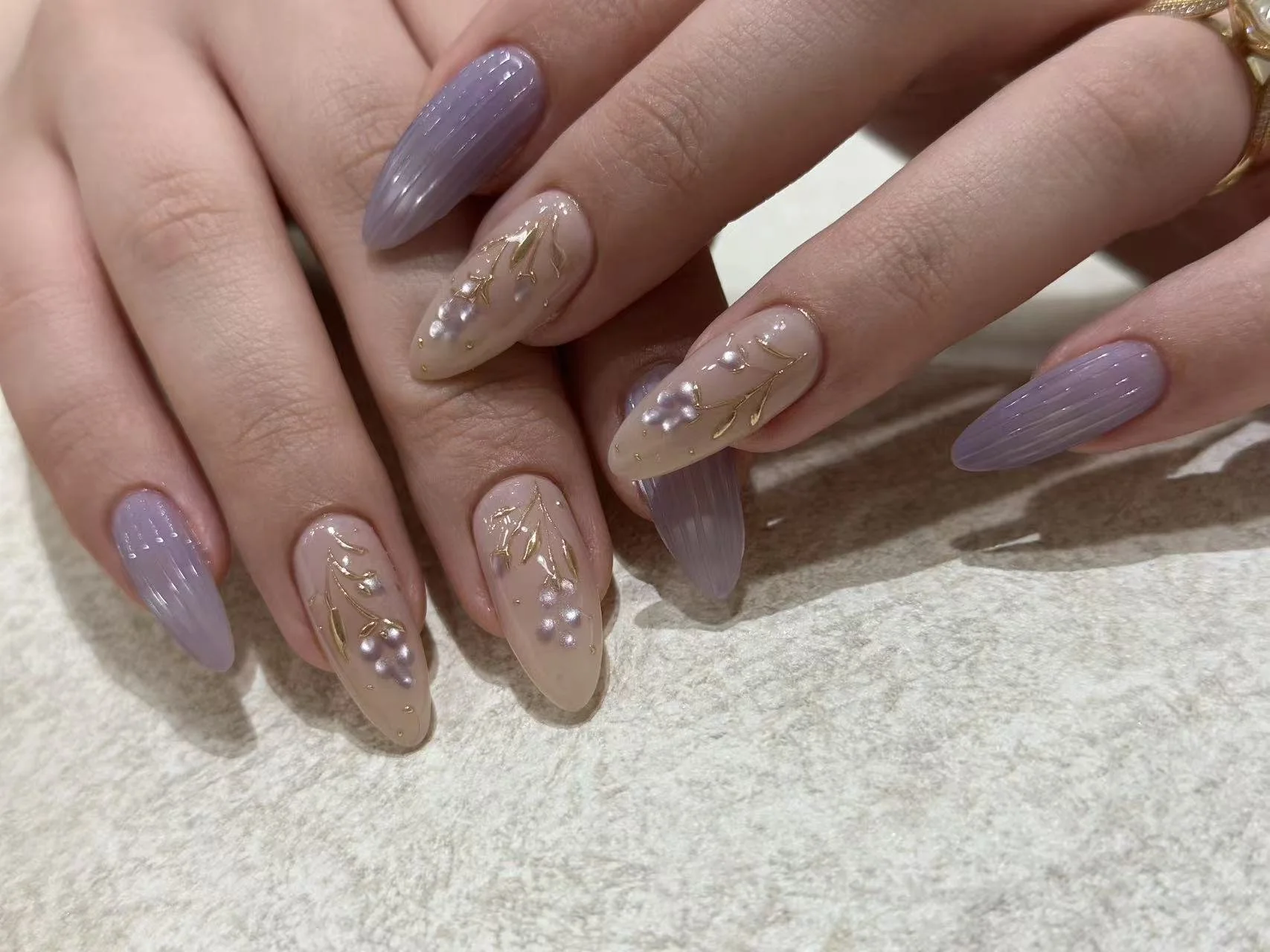 Lavender manicure with delicate gold leaf and pearl nail art accents.