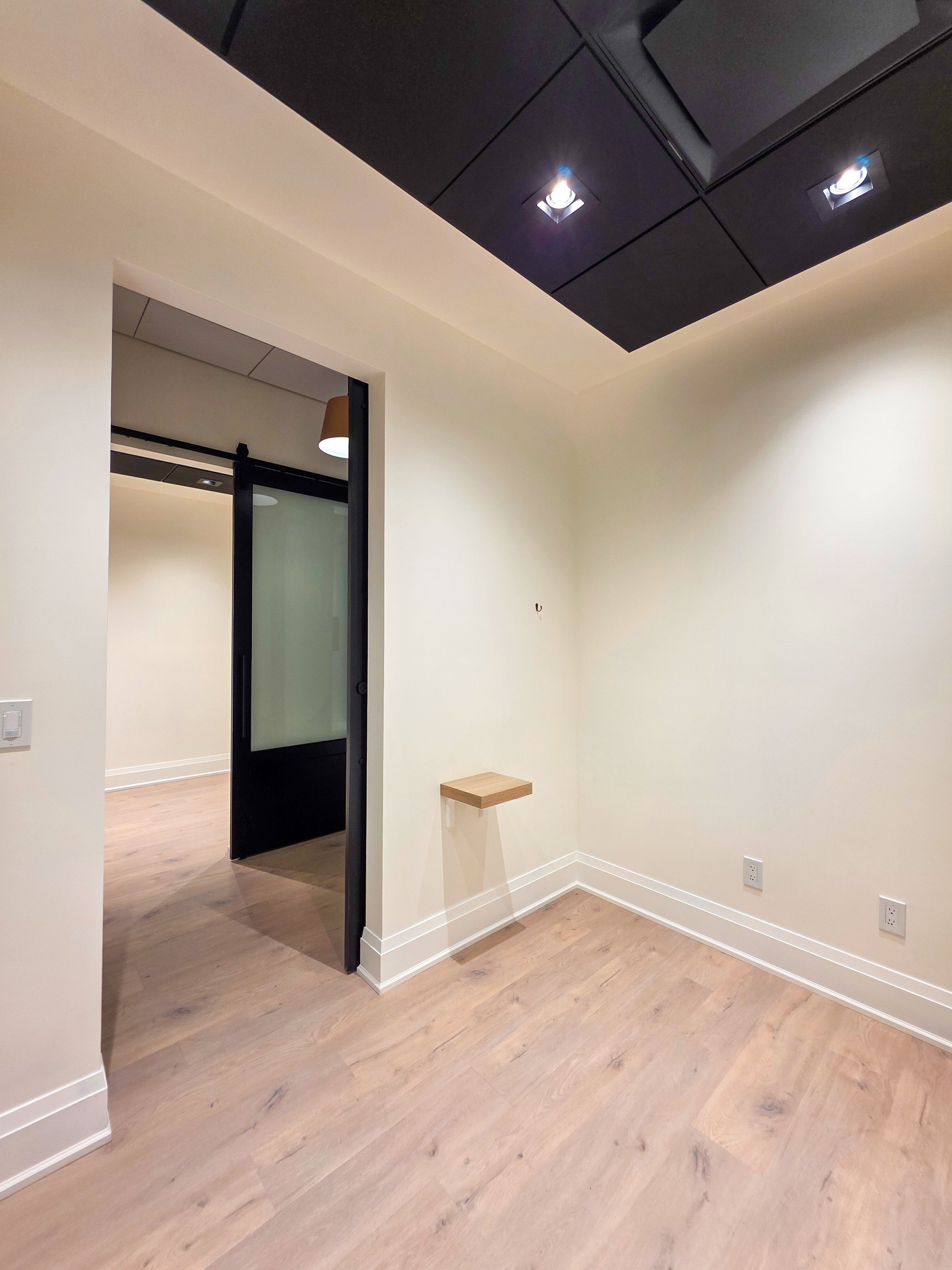 Empty room with beige walls, hardwood floors, black door frame, and several electrical outlets.