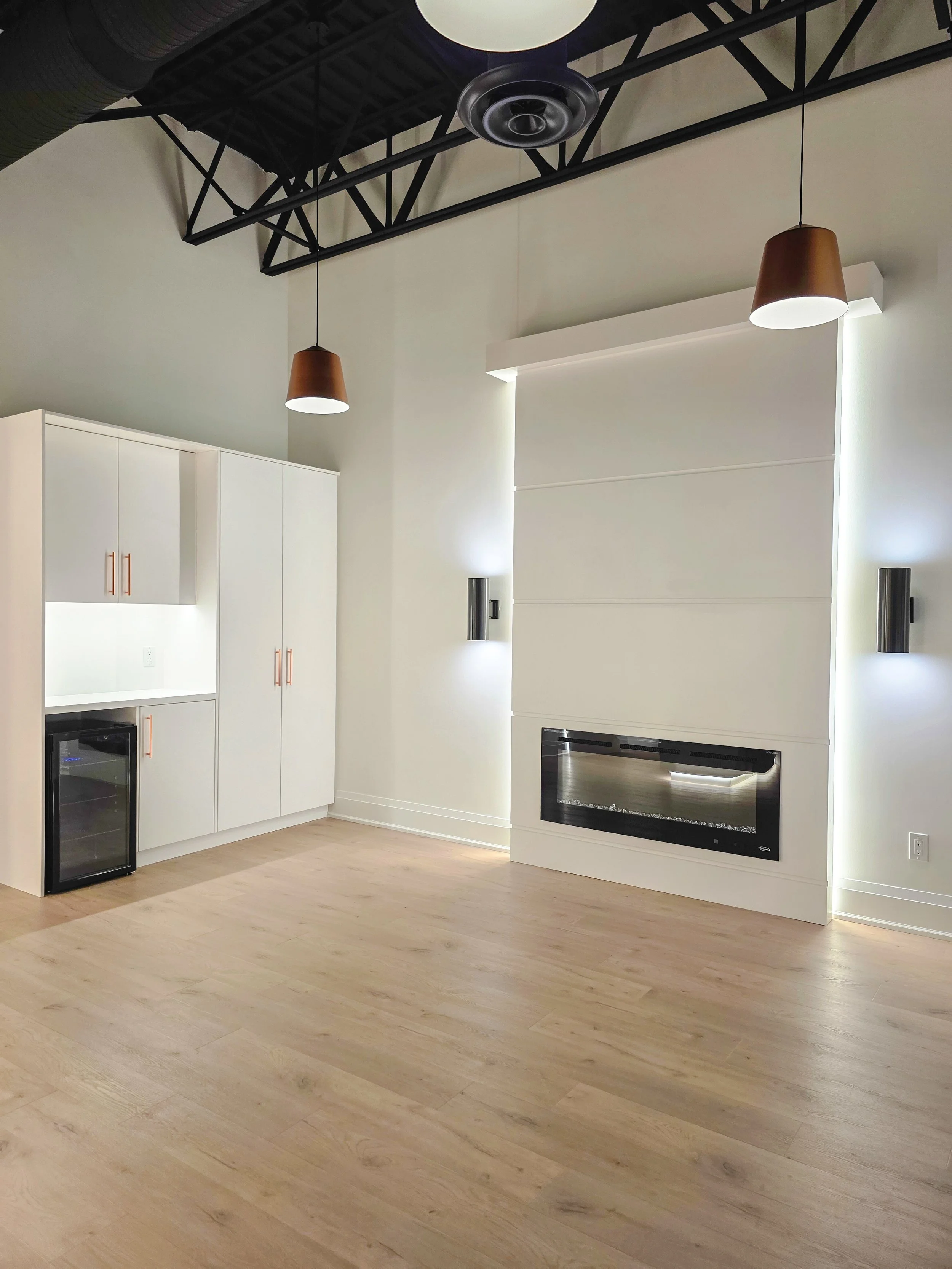 Completed a commercial tenant improvement in Orchard Plaza, Kelowna BC with white cabinets, a black wine cooler, a built-in oven, and an electric fireplace, with light wood flooring and minimalistic design.