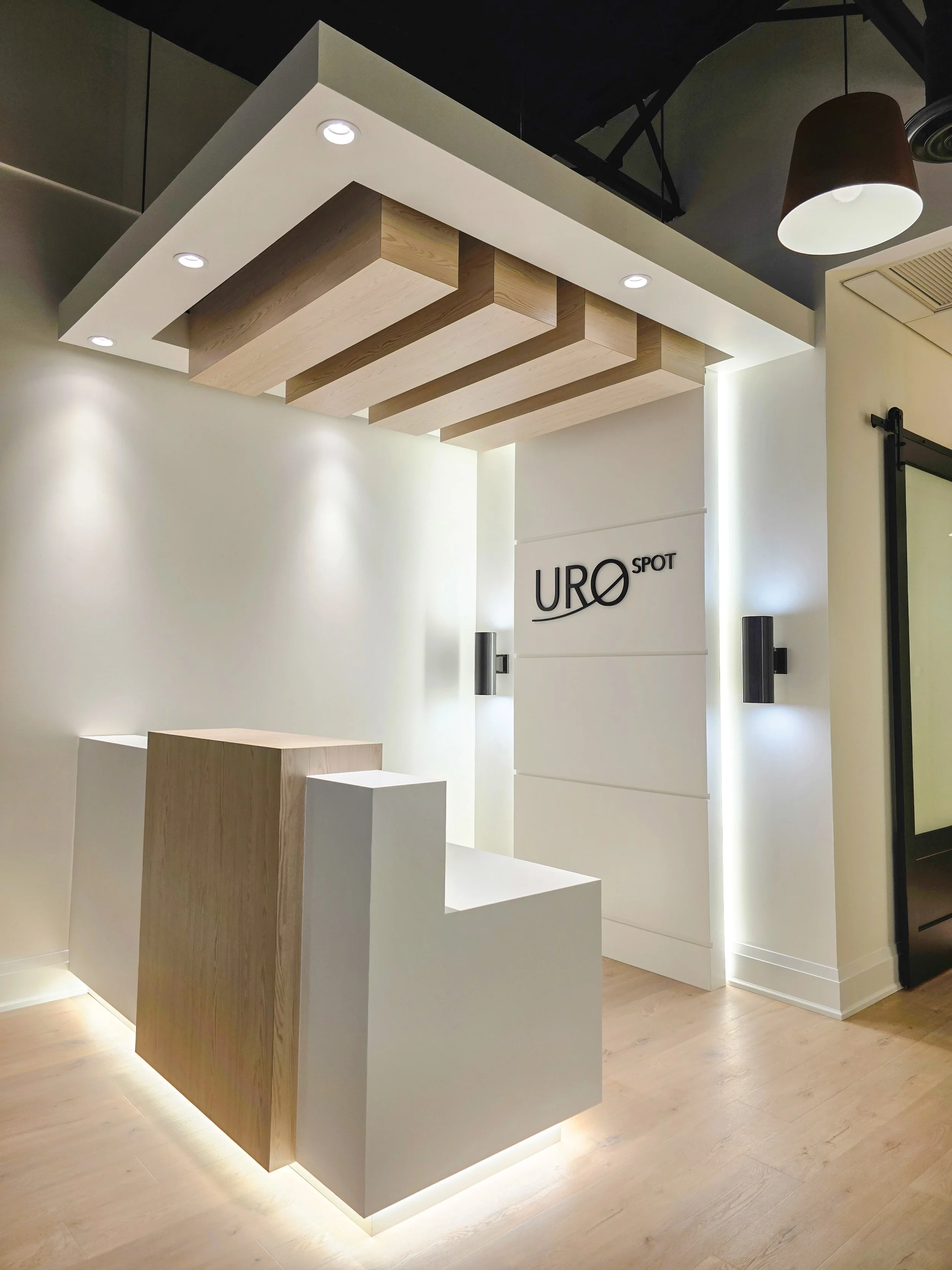 Completed a commercial tenant improvement in Orchard Plaza, Kelowna BC with modern reception desk with wooden and white surfaces under ceiling lights in UROSPOT Kelowna.