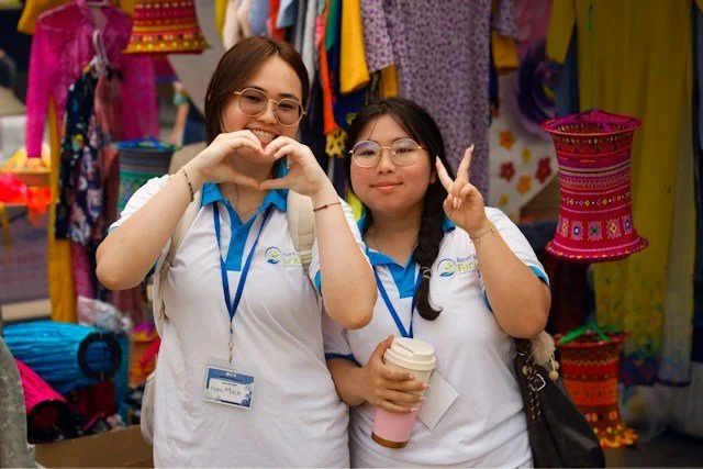 Two young women giving heart and piece signs with their hands in a market