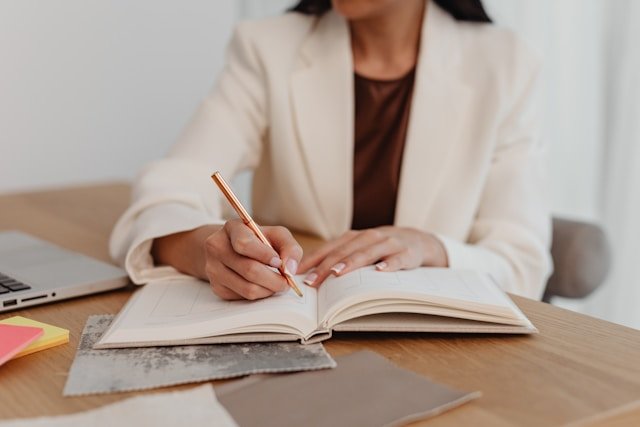 woman sitting at a desk writing on a book with a pen