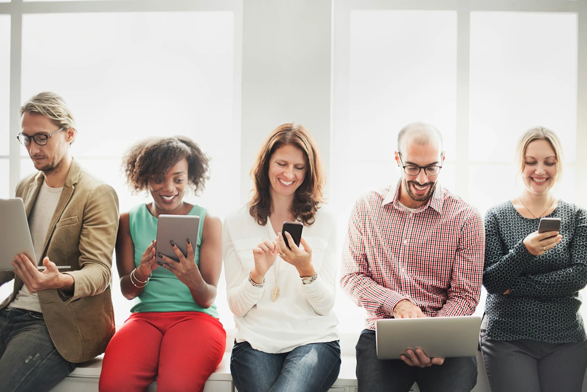 Multiple different people looking at their phones, tablets and laptops and smiling