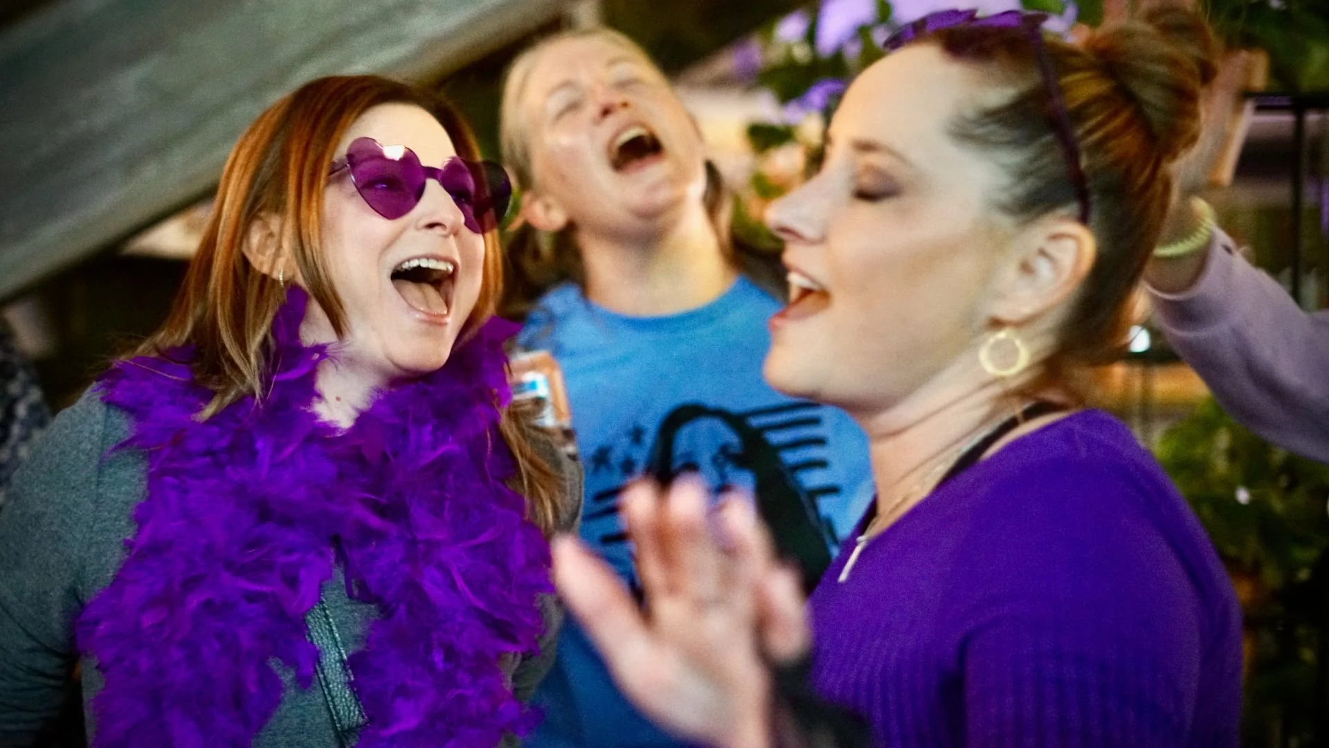 Three ladies with purple attire or accessories, having a ton of fun, dancing, eyes closed, singing passionately along with a song, living their best life!