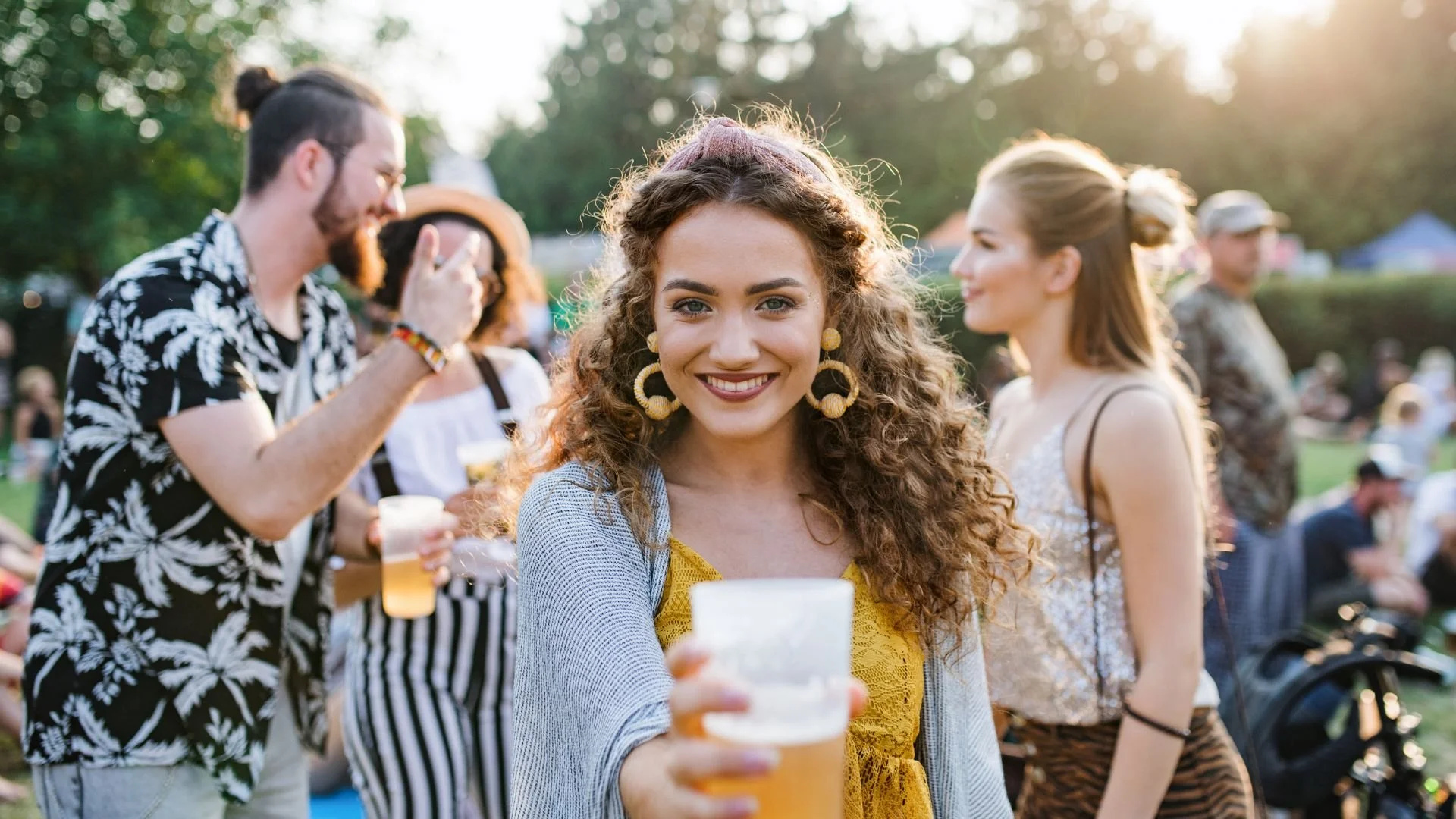 People at a festiva drinking beer, smiling and having fun outside.