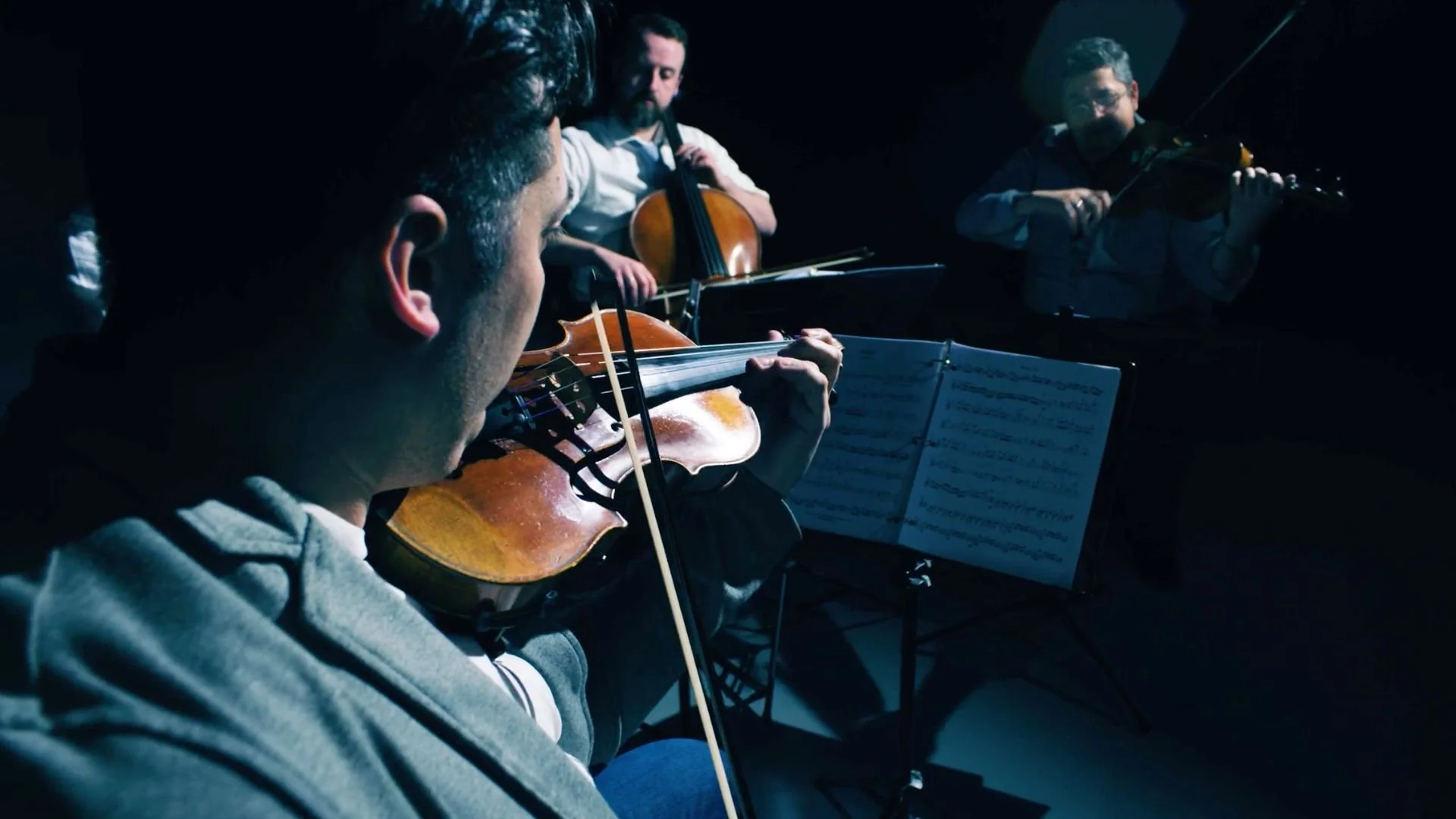 A string quartet performing in low lighting. Light fixtures illuminate the area from above..