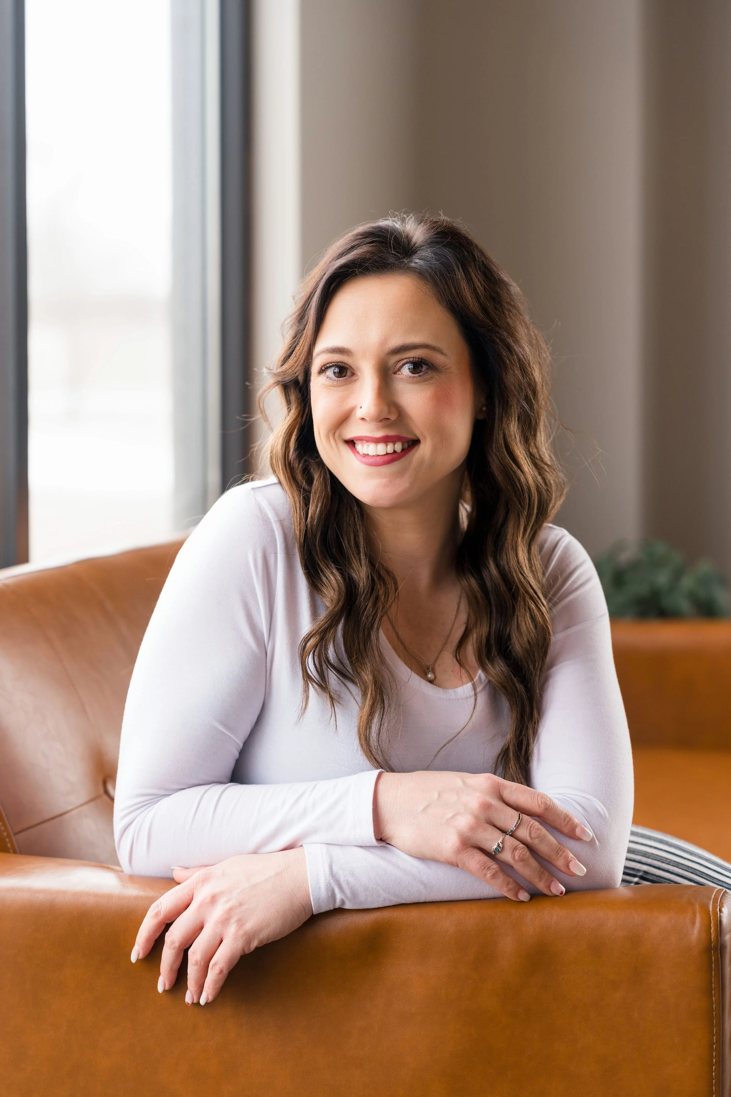 Close up of curly specialist smiling in a camel colored lobby area chair
