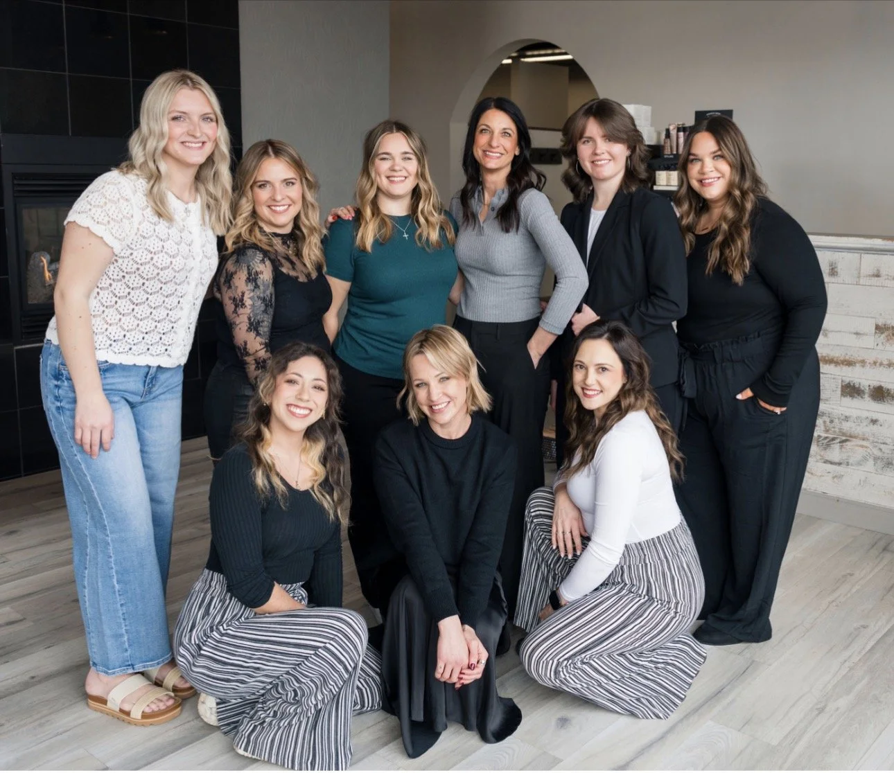Group of ten women posing indoors, smiling, with a mix of casual and business casual clothing.