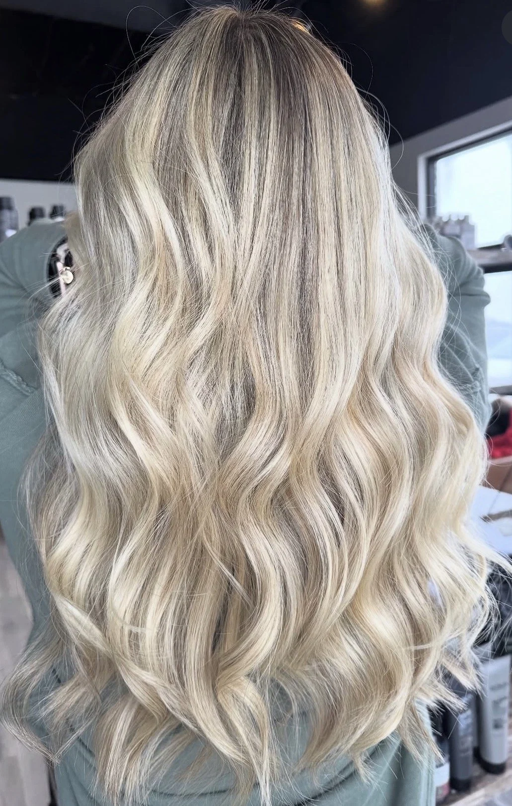 Long, wavy blonde hair with darker roots, styled in loose curls.