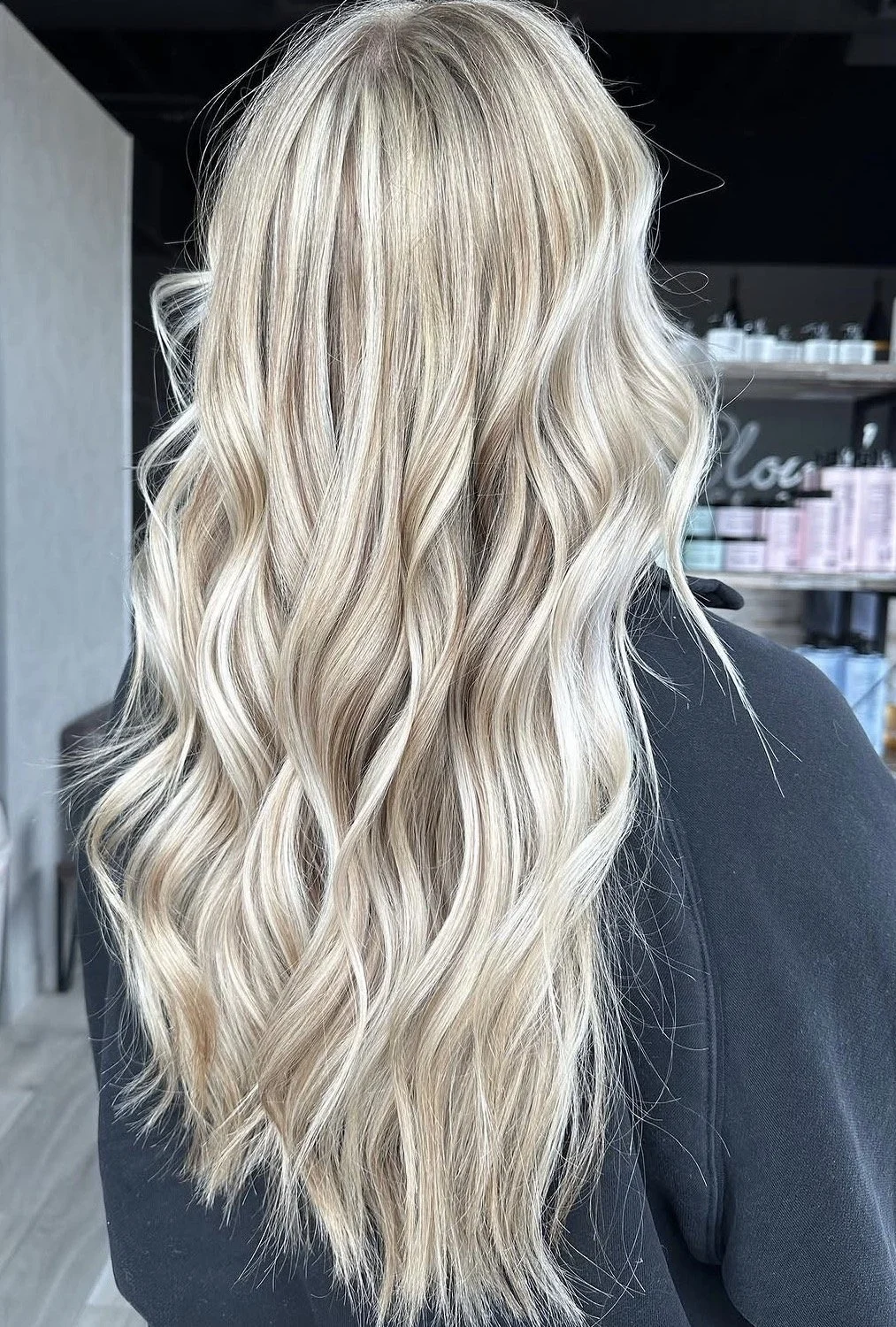 A person with long, wavy blonde hair, seen from behind in a hair salon.