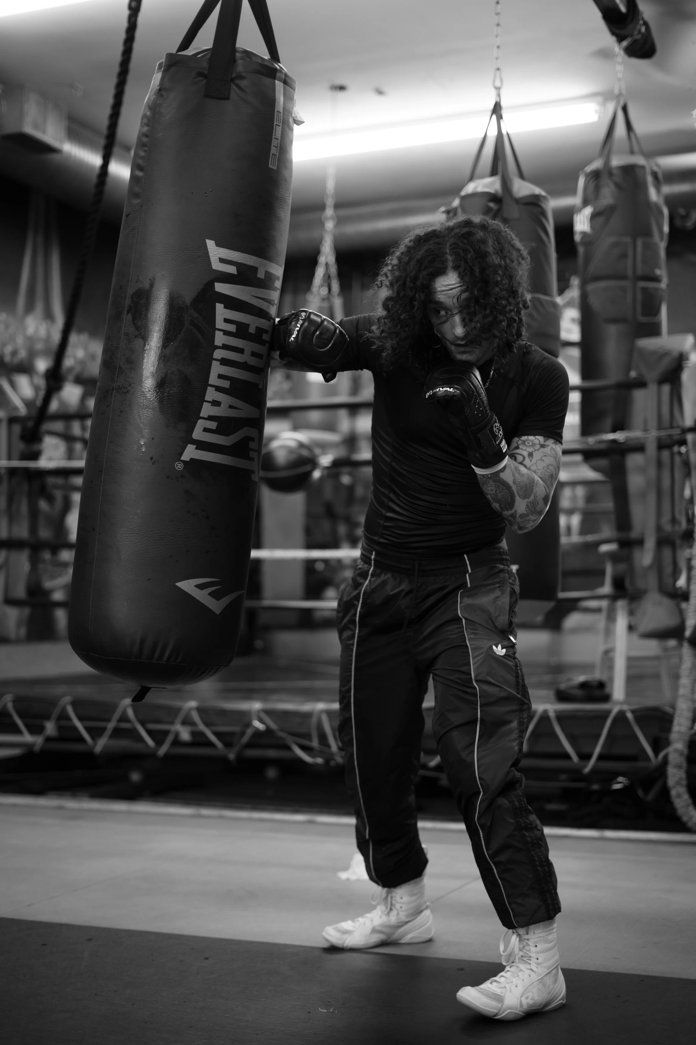 A woman with curly hair practicing boxing in a gym with punching bags.