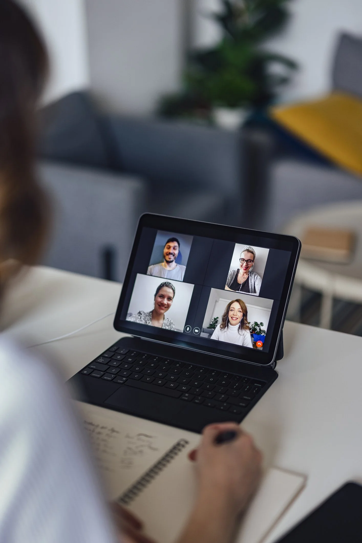 Videollamada en una tableta con cuatro participantes, uno con un cuaderno y bolígrafo sobre la mesa, recibiendo información crucial para transformar su vida de Semiología de la Vida Cotidiana compartida en un taller vivencial.