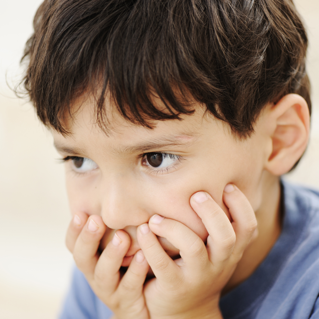 young boy holding his face with a worried, distracted expression