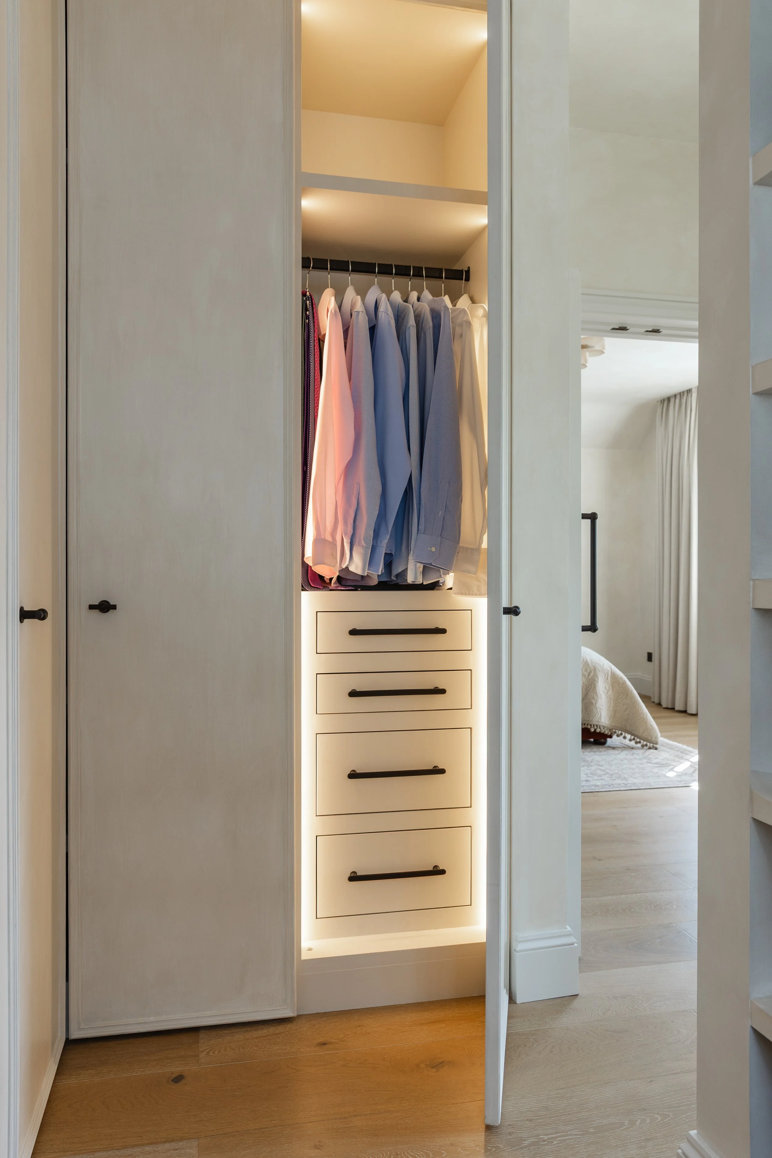 Open closet showing hanging shirts in blue, pink, purple, and white, with built-in shelves and drawers, illuminated with LED lighting.