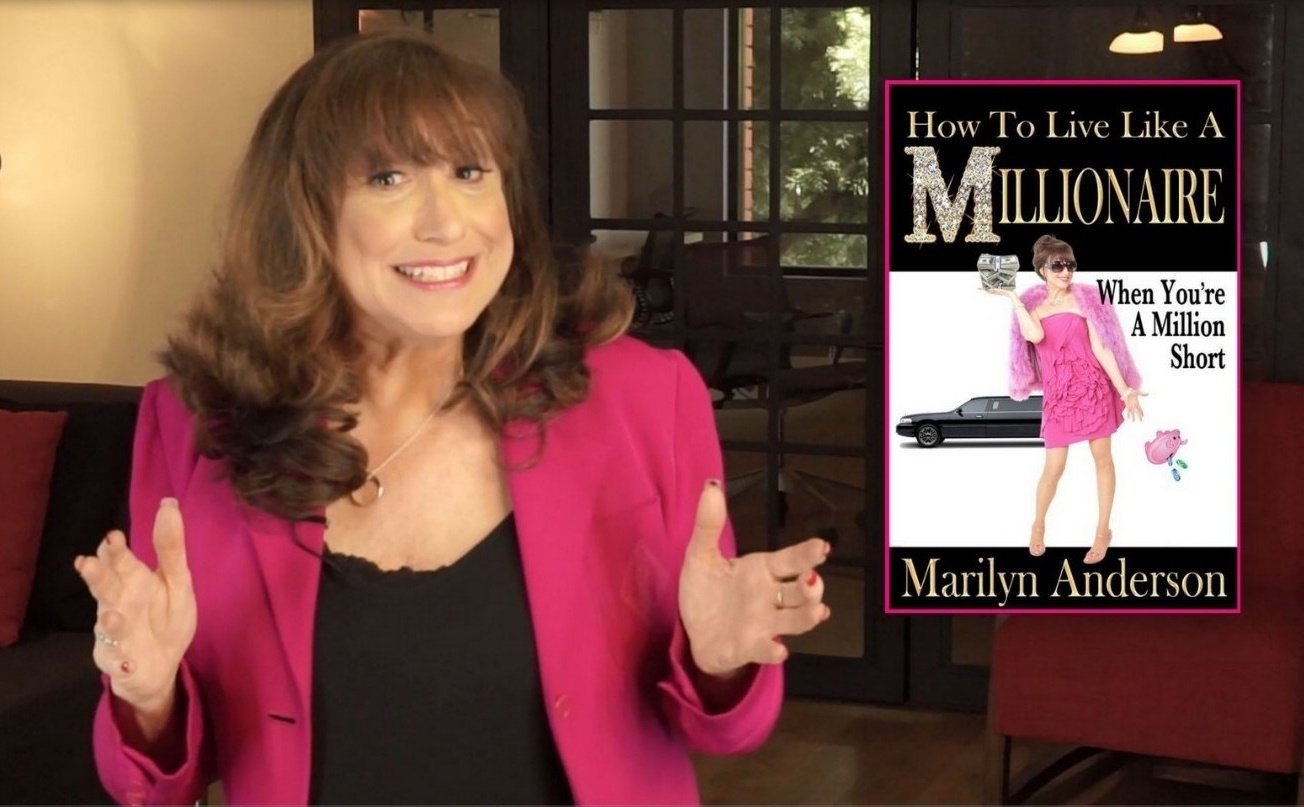 A woman with brown curly hair wearing a pink blazer and black top smiling and gesturing with her hands. To her right, a book cover titled 'How To Live Like A Millionaire When You're A Million Short' by Marilyn Anderson is visible. The book features an image of a woman in a pink dress and sunglasses holding a stack of money, with a luxury car and a piggy bank illustration.