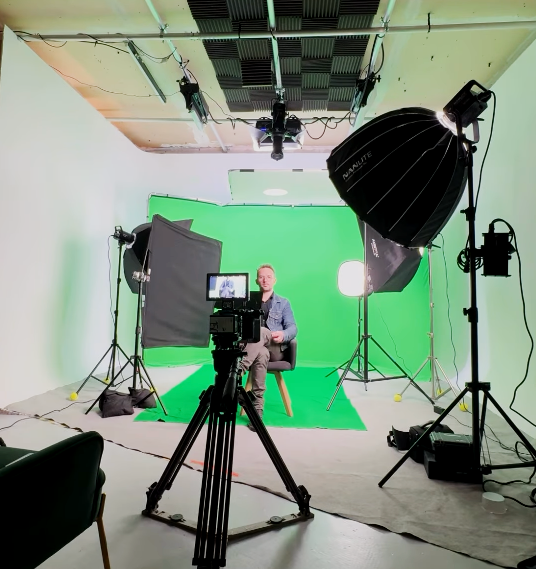 Studio de tournage Cyclorama avec un homme assis devant un écran vert, entouré d'éclairage professionnel et de caméras.