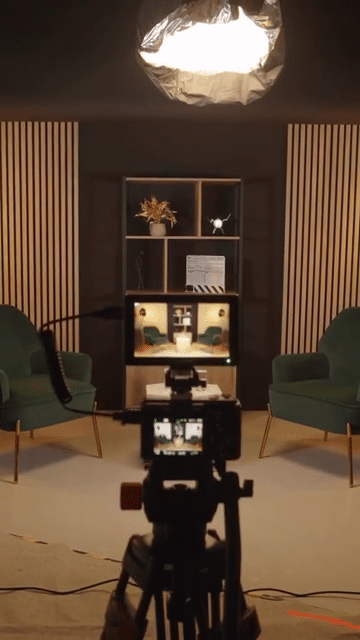 Studio d'enregistrement podcast avec deux fauteuils verts, une étagère avec décorations, dispositif d'enregistrement et caméra en avant-plan.